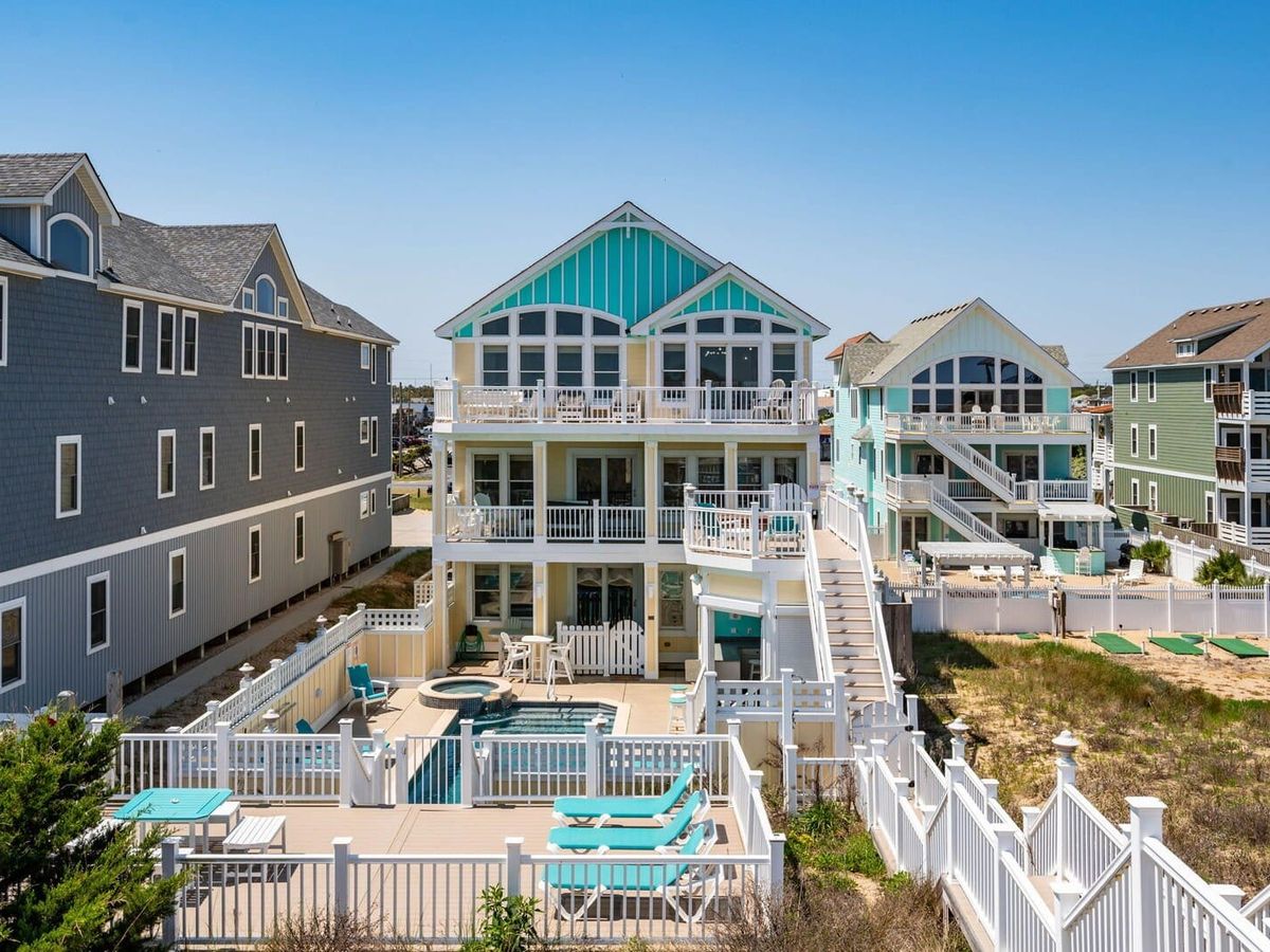 Bright blue vacation home with stairs going down and leading to private pool area with lounge chairs