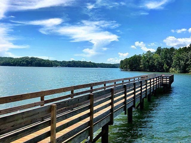 A wooden fishing dock stretches into the peaceful waters of Lake Hartwell, perfect for a quiet day of casting lines. Blue skies and calm waters make it ideal for relaxing.