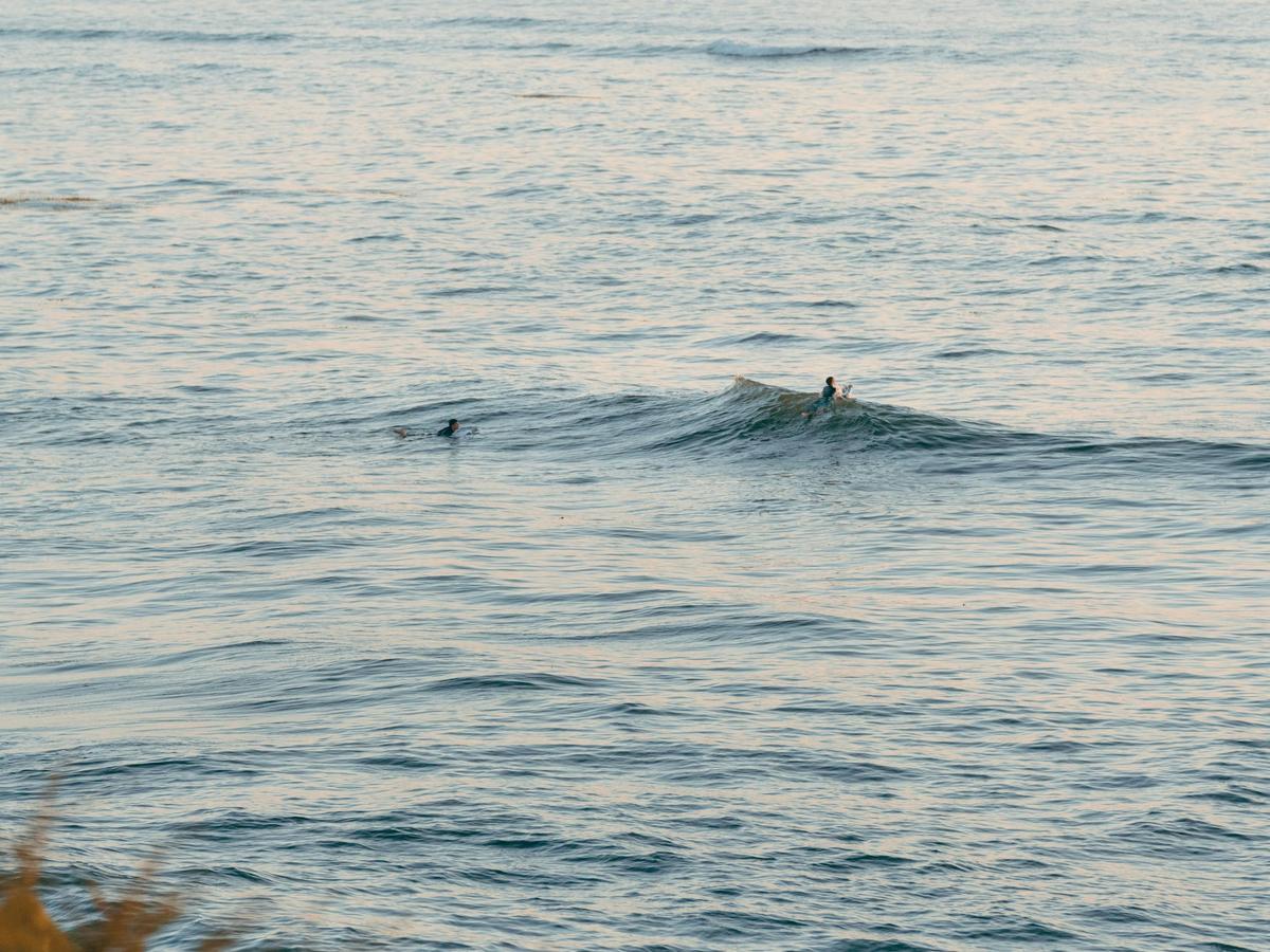 Two surfers float in calm ocean water during golden hour as soft light reflects across the sea near the San Diego coastline. The peaceful scene shows why sunset is one of the best times for beach photography in San Diego.