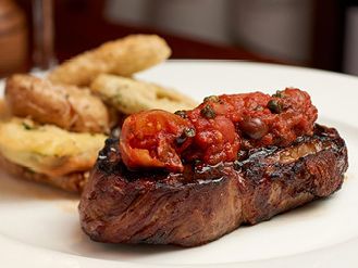 A perfectly grilled steak topped with tomato sauce and served with crispy fried zucchini at Enzo’s Hideaway. A rustic Italian-American classic.