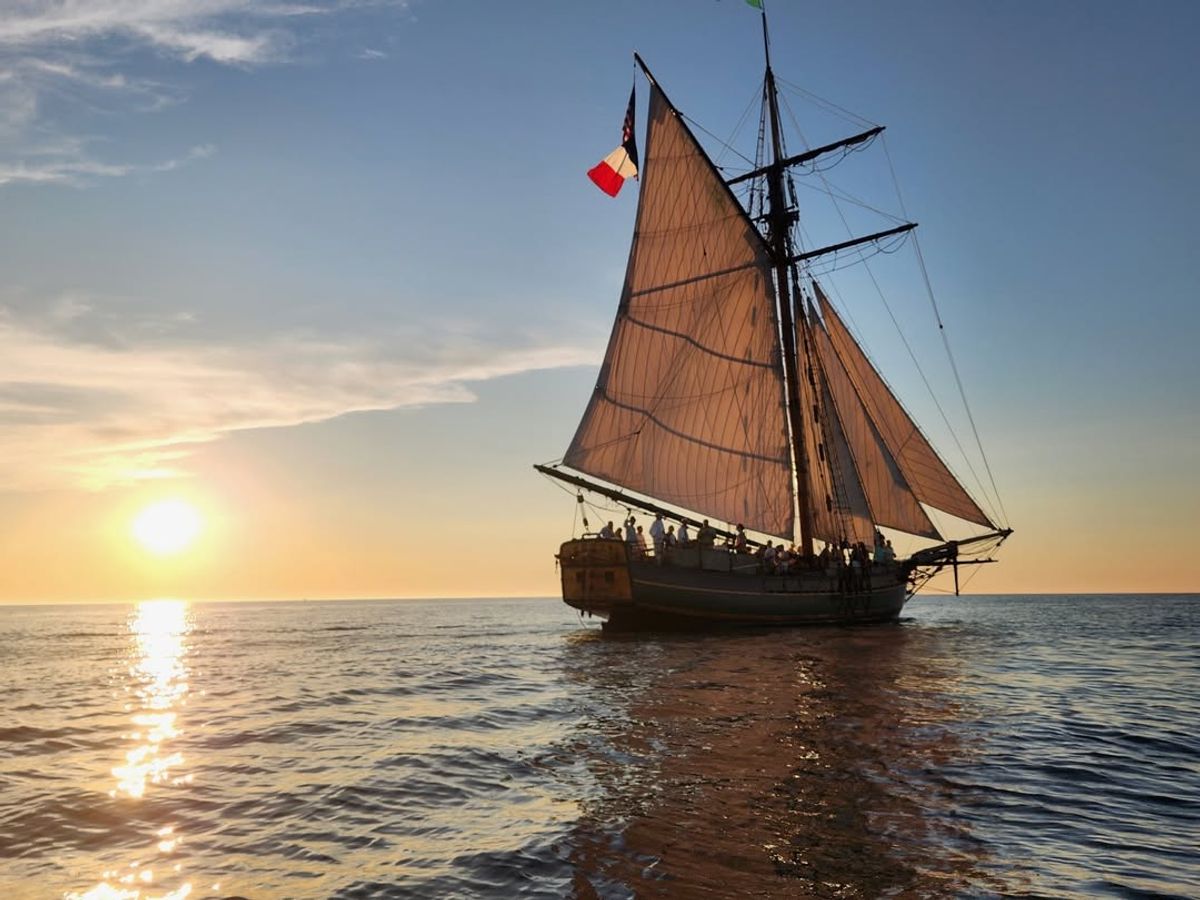 A tall ship sails gracefully on Lake Michigan as the sun sets, casting golden light across the water. Visitors can enjoy a historic sailing experience while learning about the region’s rich maritime history.