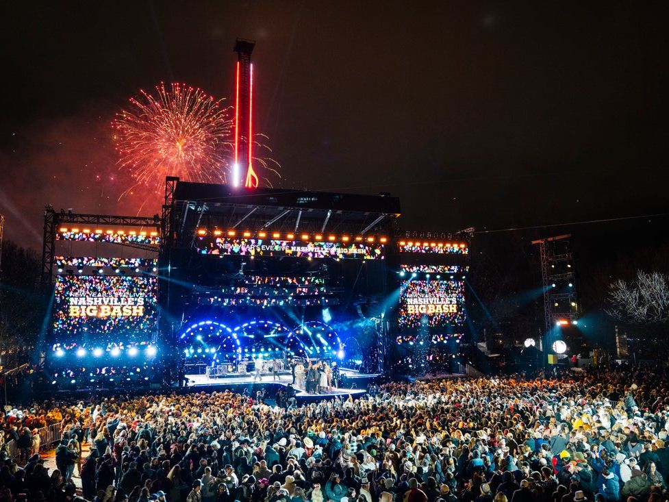 Fireworks explode above the Nashville Big Bash stage as confetti fills the air at midnight. The crowd celebrates the New Year with live performances and bright stage lights.