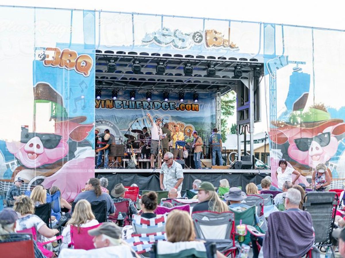 Festival goers gather in front of a live music stage during a Blue Ridge BBQ festival, enjoying outdoor seating and a lively crowd. This popular event brings together BBQ lovers, local music, and a relaxed mountain-town atmosphere.