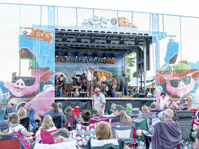 Festival goers gather in front of a live music stage during a Blue Ridge BBQ festival, enjoying outdoor seating and a lively crowd. This popular event brings together BBQ lovers, local music, and a relaxed mountain-town atmosphere.