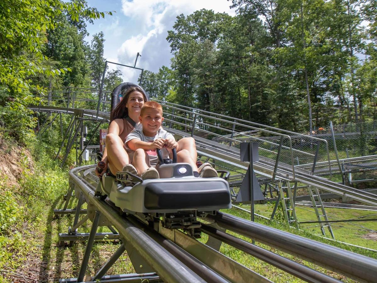 A mom and her young son enjoy an exciting ride down the Rocky Top Mountain Coaster surrounded by lush green trees. The coaster’s metal tracks curve through the Smoky Mountain forest for a fun family adventure.