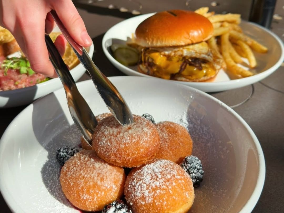 A sunny brunch table with powdered beignets, fresh blackberries, and a juicy burger with fries. A perfect sweet and savory combo for weekend cravings.