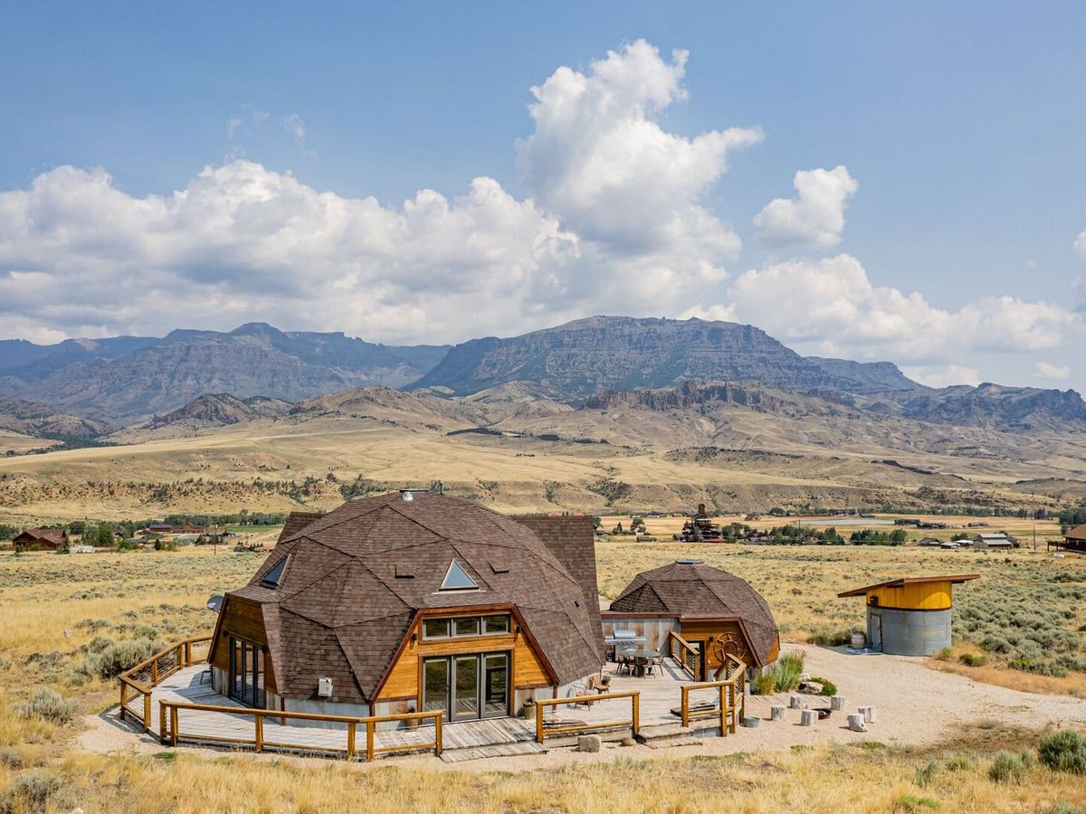 Dome house with wooden fence next to smaller dome house and in the background mountains and clouds