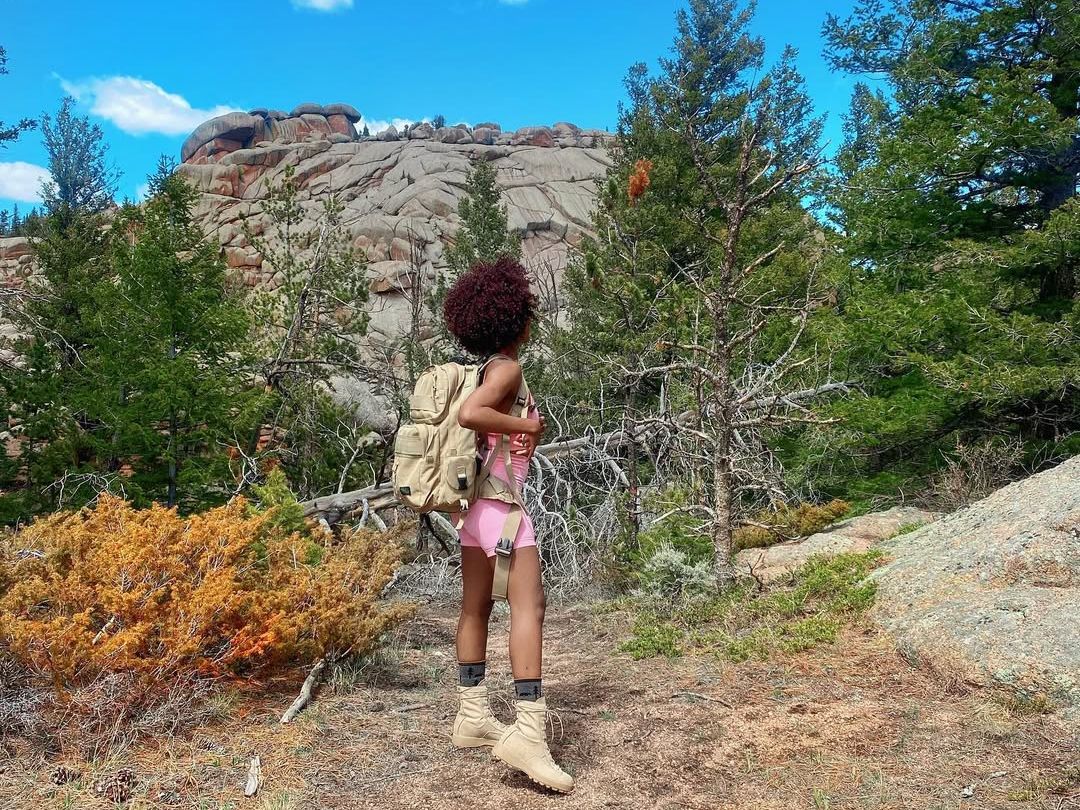 A hiker with a backpack pauses on the trail at Vedauwoo, surrounded by pine trees and dramatic granite rock formations. This spot in Wyoming is popular for climbing, hiking, and exploring unique high-desert landscapes.