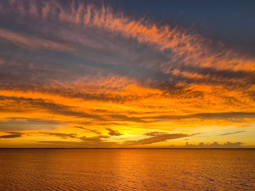 A breathtaking sunset lights up the sky in shades of gold and orange over calm ocean waters. This view reflects the warm, welcoming spirit of Cocoa Beach, where every evening ends in color and calm.