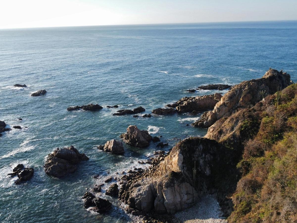 Rocky coastal cliffs overlook the deep blue ocean with waves crashing against the shore. The rugged landscape and clear horizon create a peaceful seaside view. This scenic coastline highlights the natural beauty of Mexico’s Pacific coast.