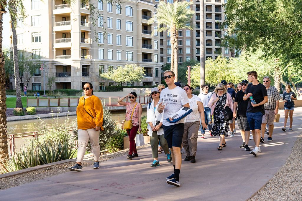 A lively group strolls along a sunny canal path, enjoying a guided food tour through the city. The mix of modern architecture and palm trees creates the perfect urban backdrop for tasting and exploring.