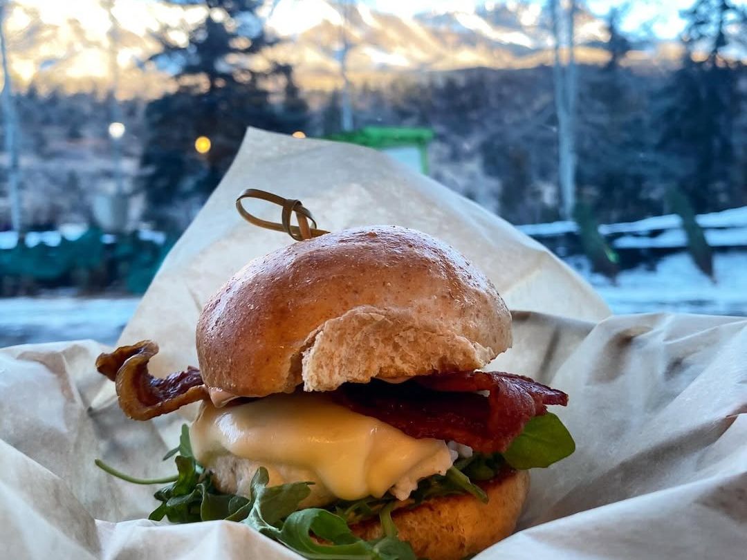 Fresh sandwich with crispy bacon, melted cheese, and arugula served on a soft bun. A casual and hearty meal set against the backdrop of Telluride’s mountain scenery.