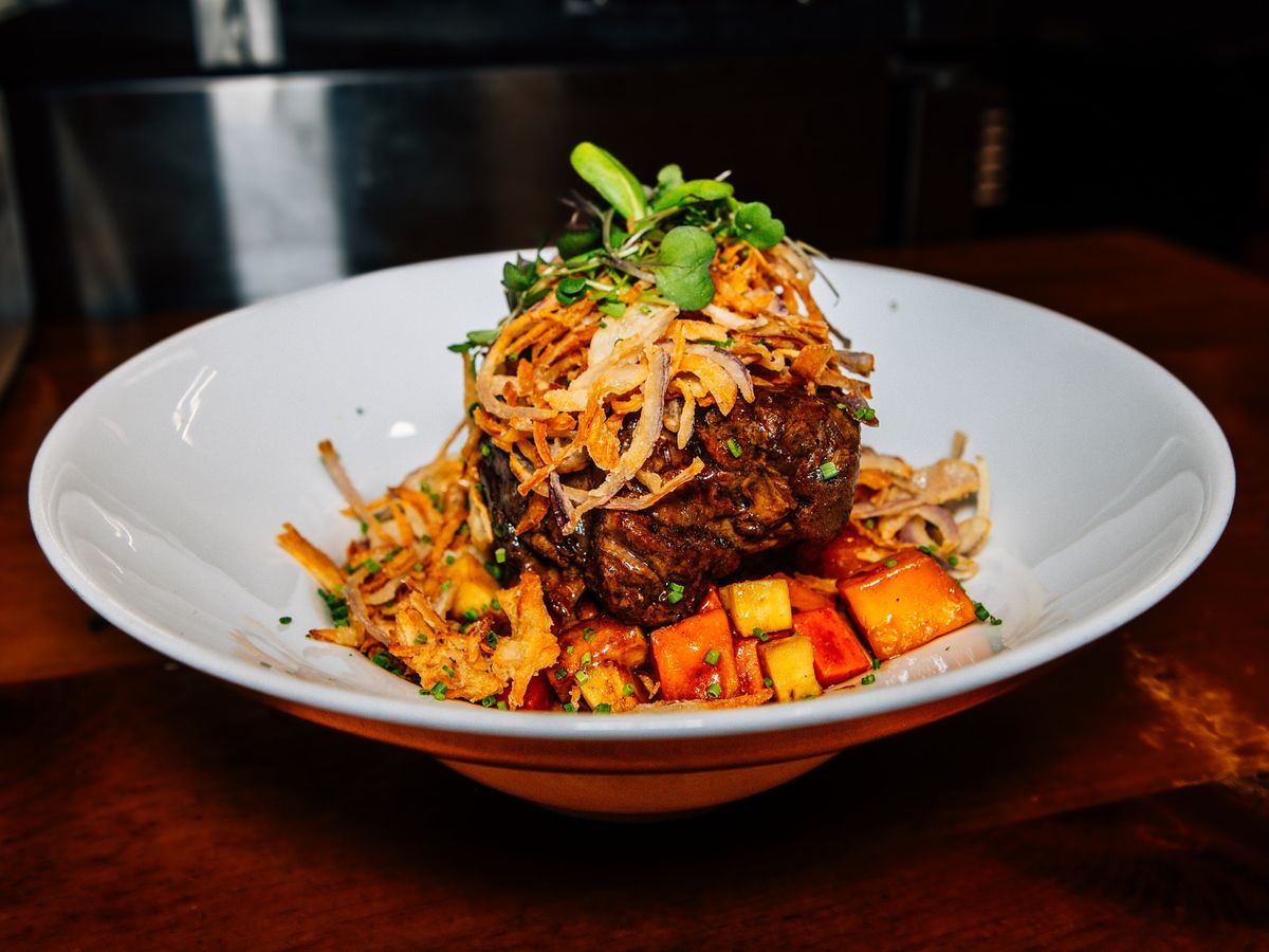 Tender braised short ribs topped with crispy onions and fresh microgreens at Wobbly Barn. Served with roasted vegetables in a rich glaze, this dish highlights bold flavors and hearty portions. Wobbly Barn in Killington is a favorite for steakhouse classics and après-ski dining.
