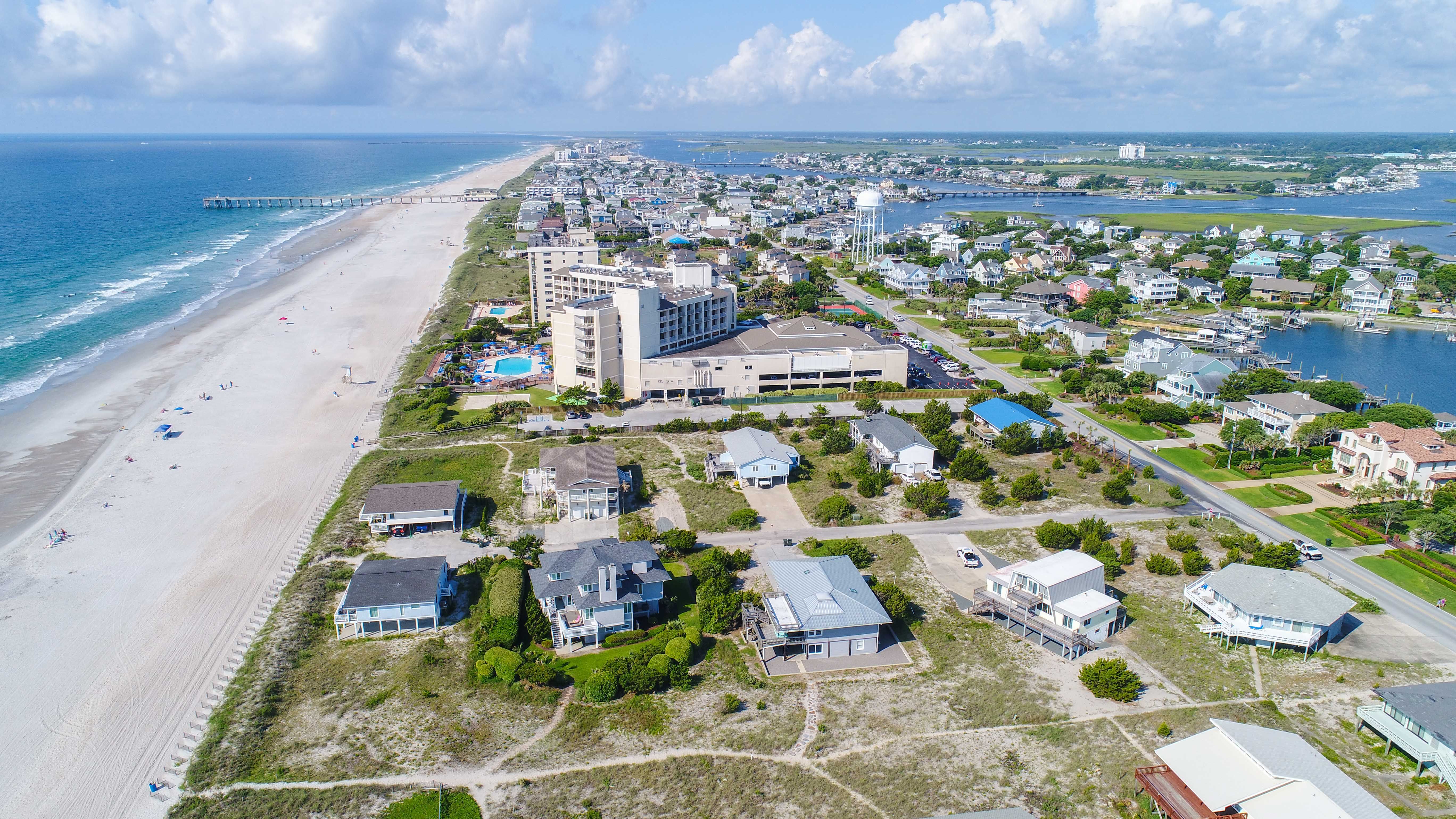 Aerial view of Wrightsville Beach, North Carolina, showing a long stretch of sandy shoreline, oceanfront homes, a pier, and vibrant coastal neighborhoods bordered by the Atlantic Ocean and inland waterways.