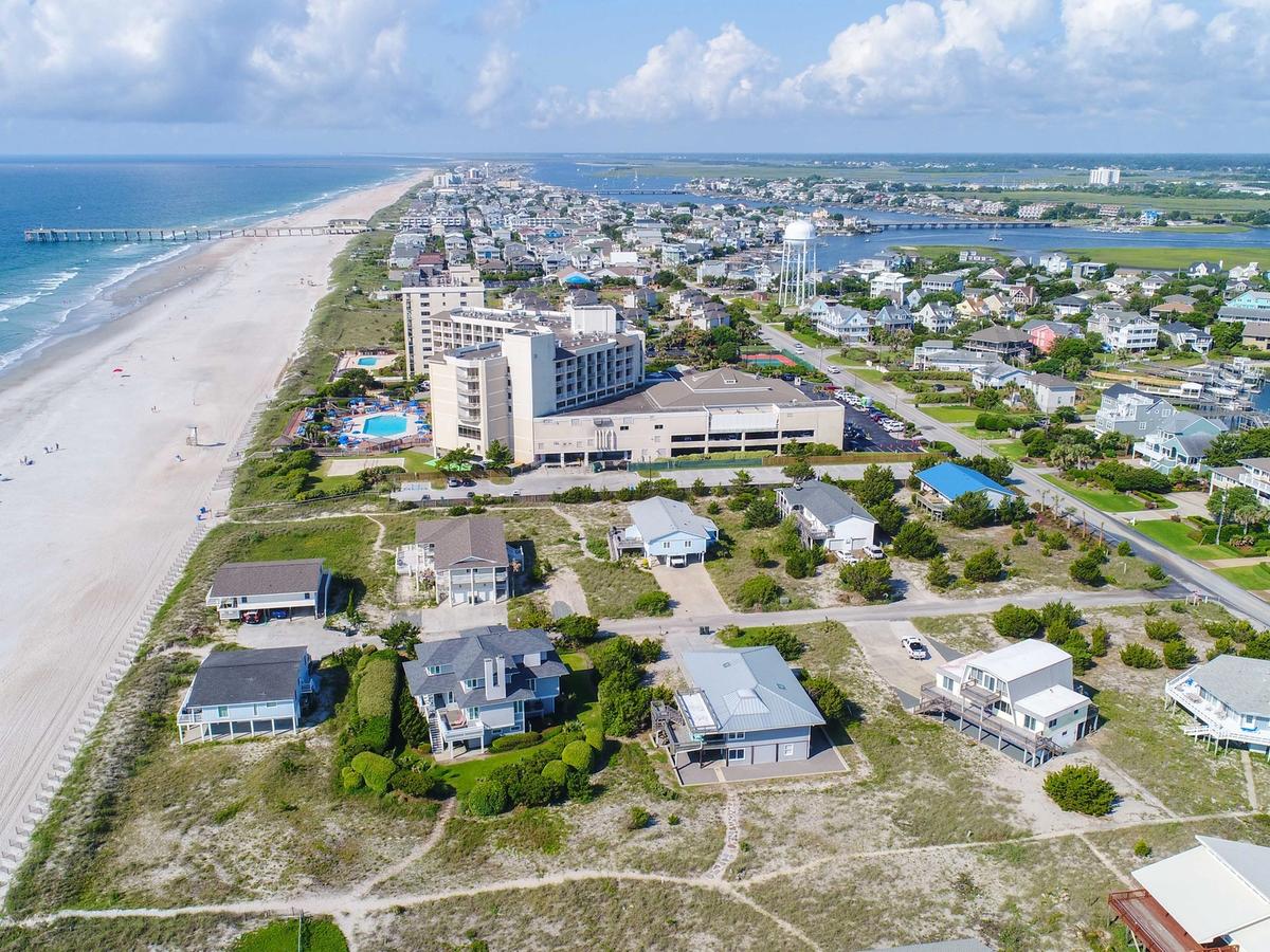 Aerial view of Wrightsville Beach, North Carolina, showing a long stretch of sandy shoreline, oceanfront homes, a pier, and vibrant coastal neighborhoods bordered by the Atlantic Ocean and inland waterways.