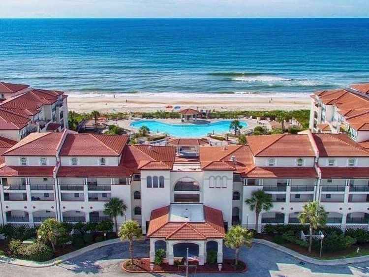 An oceanfront resort with red rooftops overlooks a sparkling beach and large pool. This peaceful spot offers amazing views and easy beach access for a perfect North Carolina getaway.