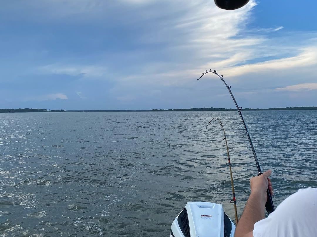 A fisherman holds two bent rods while waiting for a bite off the coast, capturing the thrill of Folly Beach Fishing Charters’ adventures on open water.