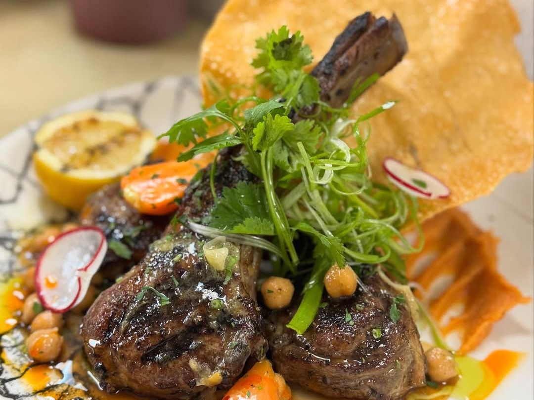 A hearty steak sandwich served with crispy fries and fresh greens on a wooden table. The dish highlights the bold flavors and generous portions many local restaurants offer. It’s the kind of comfort food that pairs perfectly with a casual lunch or dinner out.