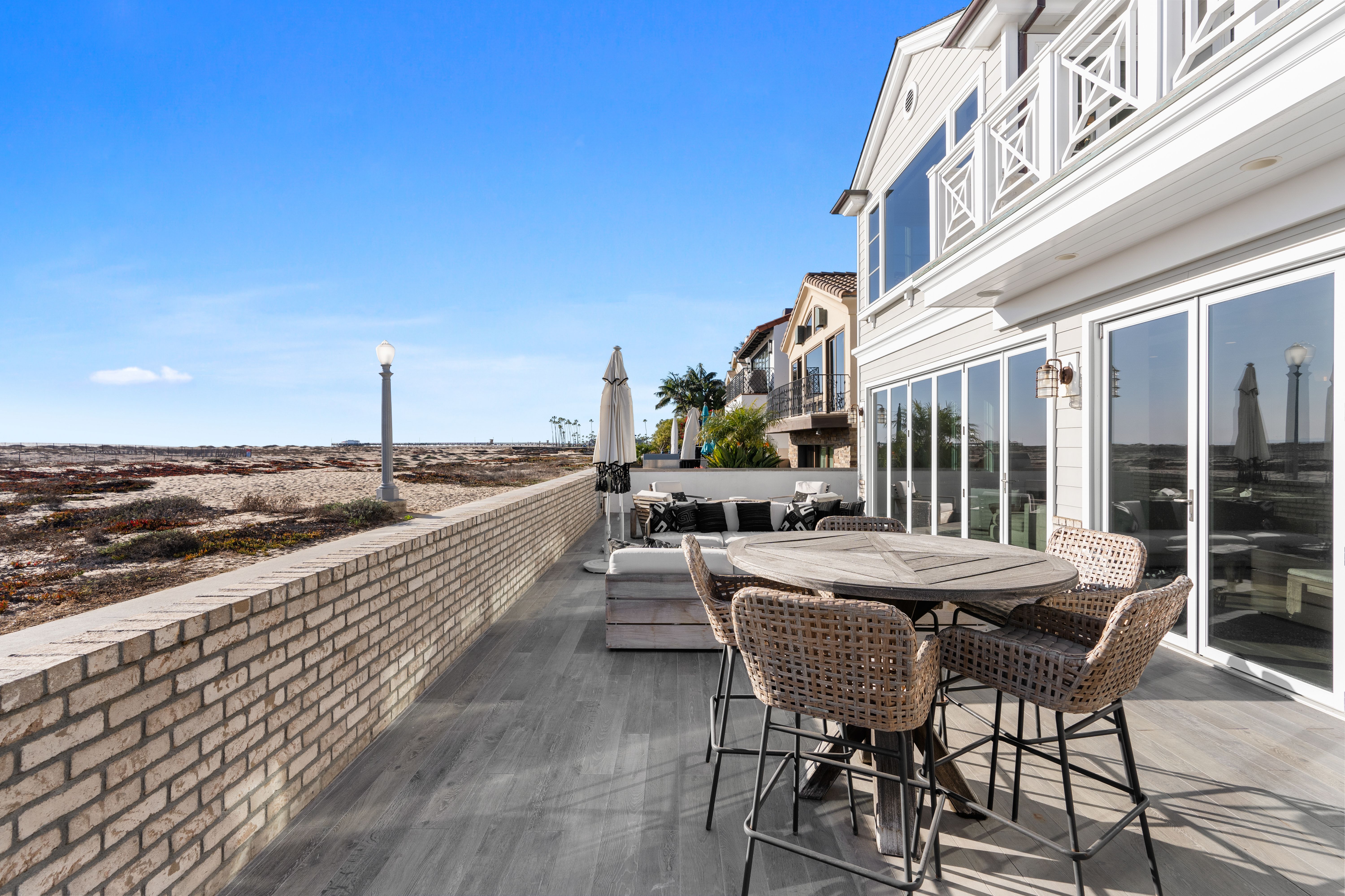Luxury oceanfront Newport Beach vacation rental with direct beach access, spacious outdoor patio, modern wicker furniture, and panoramic coastal views.