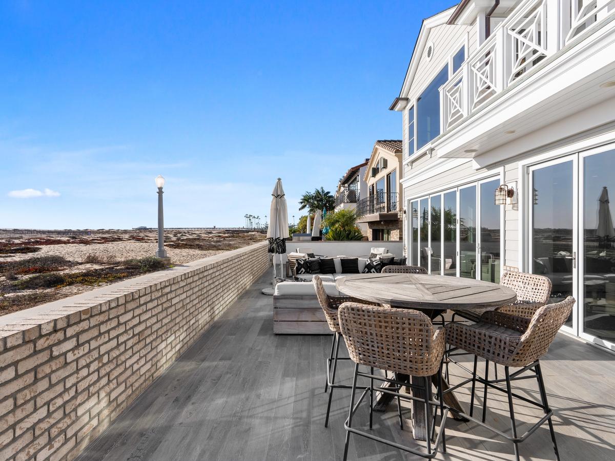 Luxury oceanfront Newport Beach vacation rental with direct beach access, spacious outdoor patio, modern wicker furniture, and panoramic coastal views.