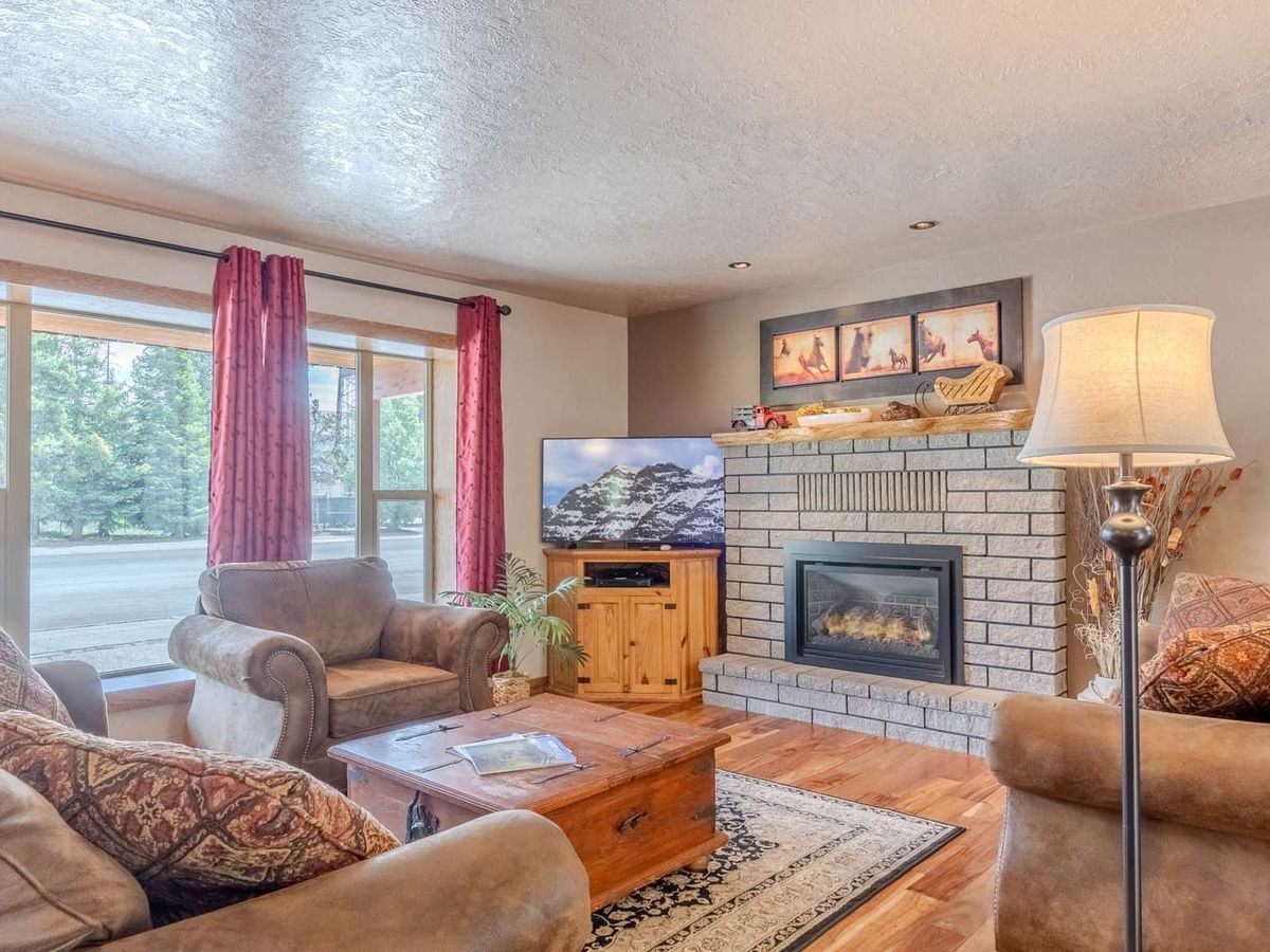 Cozy living room with large windows, warm-toned furniture, and a brick fireplace topped with rustic decor.