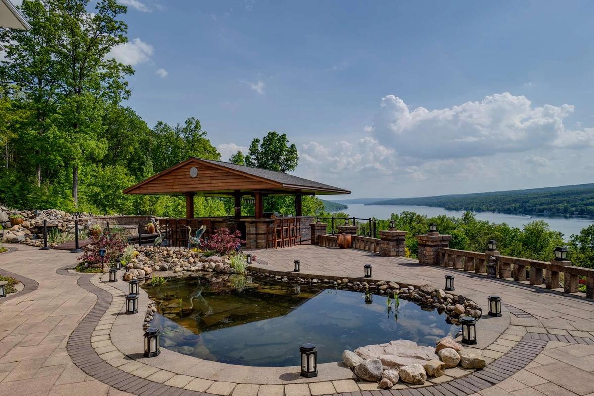 A scenic stone patio at The Villa on Esperanza featuring a peaceful water feature and an outdoor bar overlooking the Finger Lakes. This luxury retreat offers wide lake views, quiet outdoor spaces, and the perfect setting for sunset drinks and relaxed evenings with your group.