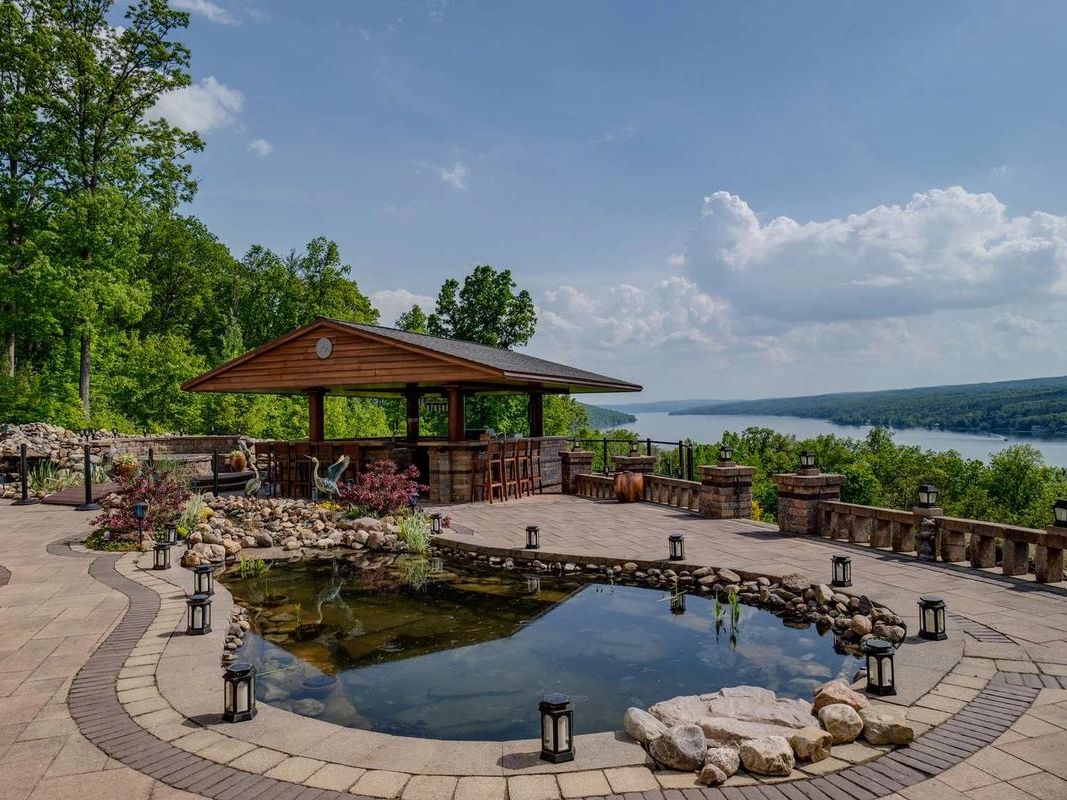 A scenic stone patio at The Villa on Esperanza featuring a peaceful water feature and an outdoor bar overlooking the Finger Lakes. This luxury retreat offers wide lake views, quiet outdoor spaces, and the perfect setting for sunset drinks and relaxed evenings with your group.