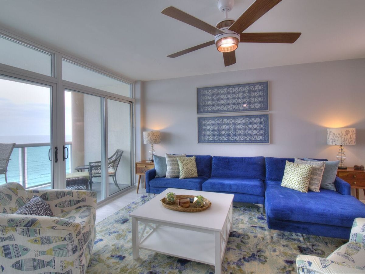 Colorful and comfy beach condo with a bright blue sectional, fun patterns, and a balcony overlooking the ocean. This is the perfect hangout spot after a beach day with the whole crew.