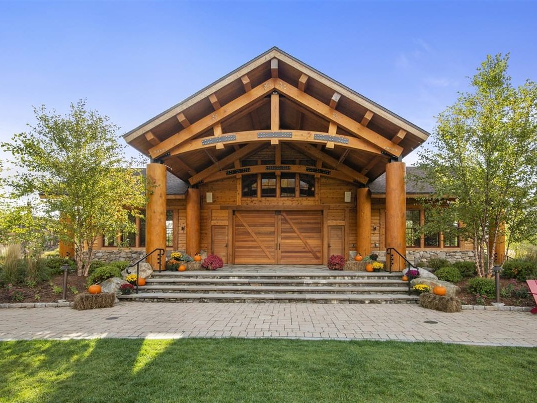 Alpine Elegance 47C features a grand timber entrance with natural wood beams, stone details, and landscaped grounds. The lodge-style design creates a warm welcome for a relaxing stay in Stowe, Vermont.