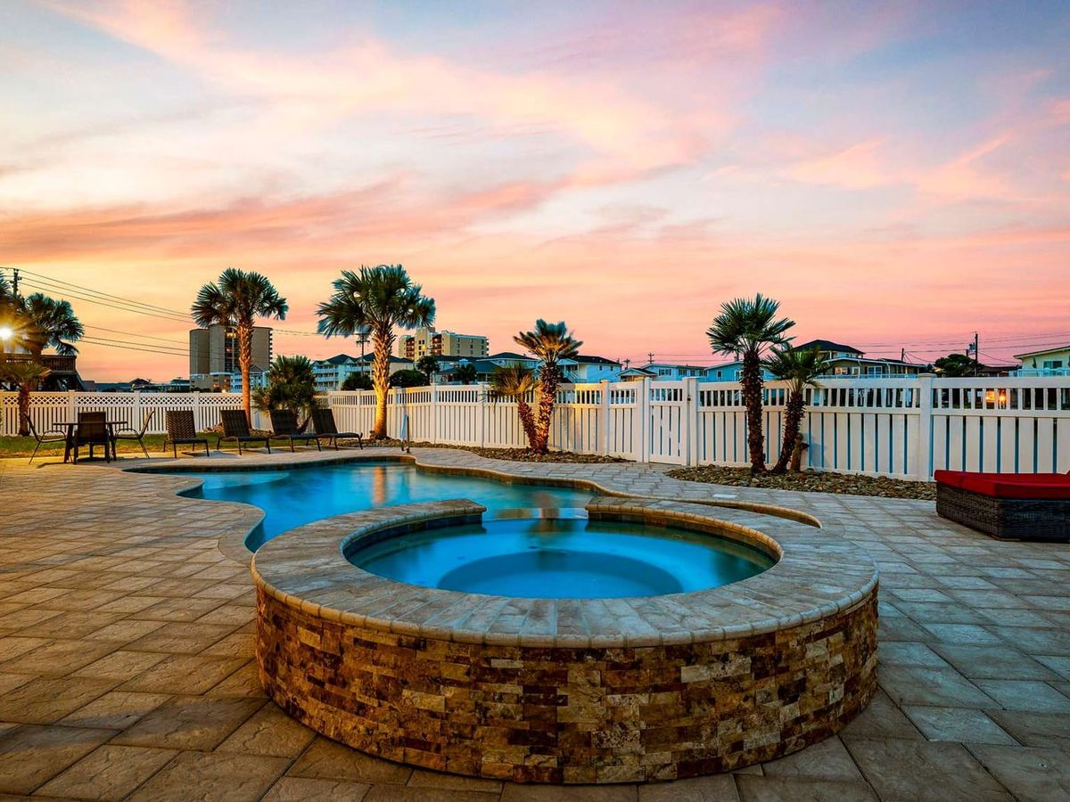 Private outdoor pool and hot tub glow beautifully at sunset, creating a relaxing backyard retreat. Lounge chairs and palm trees add a tropical feel, perfect for evening swims after a beach day.
