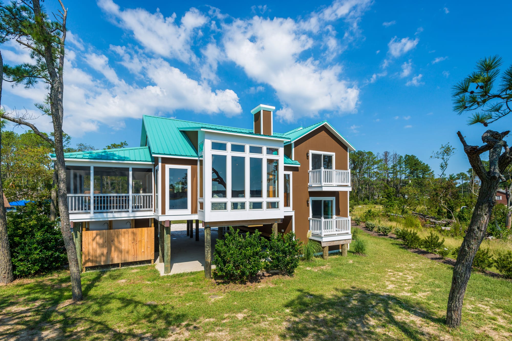 A coastal retreat with teal roofs and white balconies surrounded by open skies and green landscape. This bright and breezy home embodies island living at its best on Chincoteague Island.