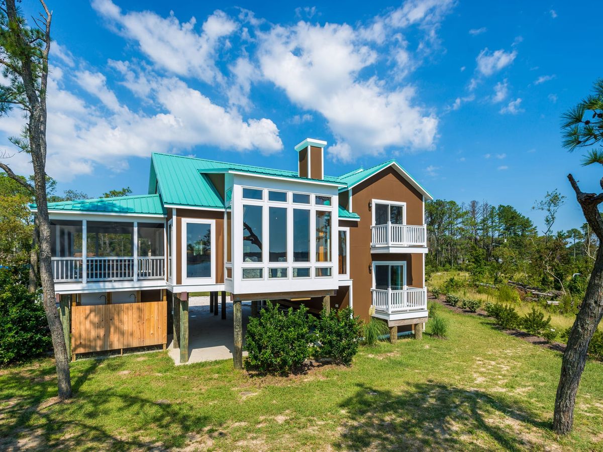 A coastal retreat with teal roofs and white balconies surrounded by open skies and green landscape. This bright and breezy home embodies island living at its best on Chincoteague Island.
