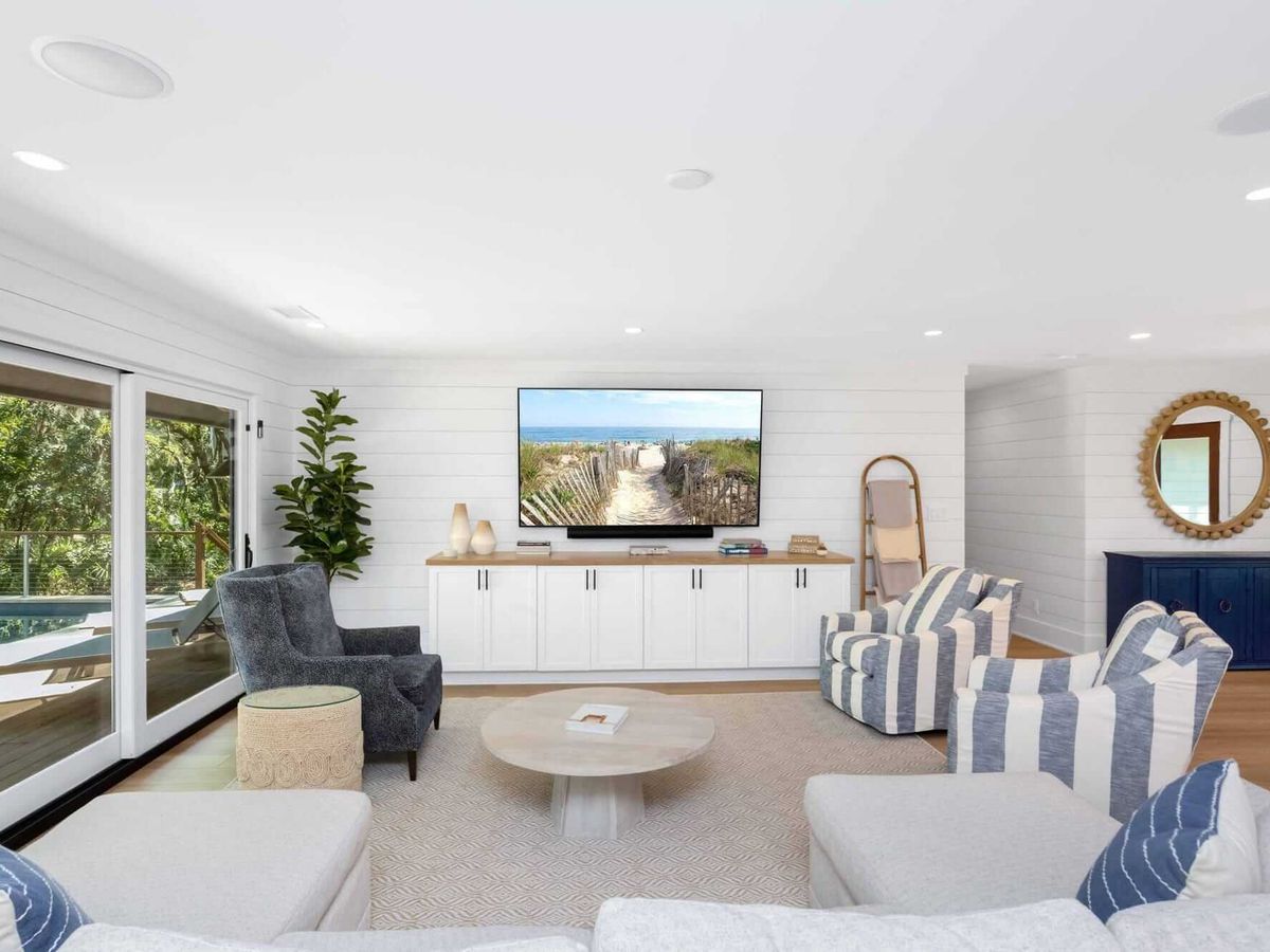 A breezy and bright entertainment space with shiplap walls and stylish furniture, just steps from the private pool deck and surrounded by lush trees.