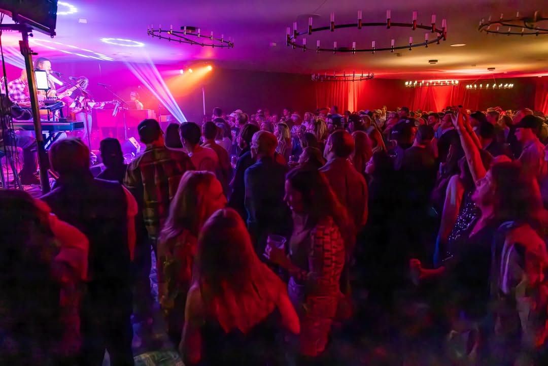 A packed crowd enjoys a live band performance at The Virginian Saloon, with colorful stage lights filling the room. This iconic Jackson Hole bar is known for its high-energy concerts, local music scene, and lively nightlife atmosphere.
