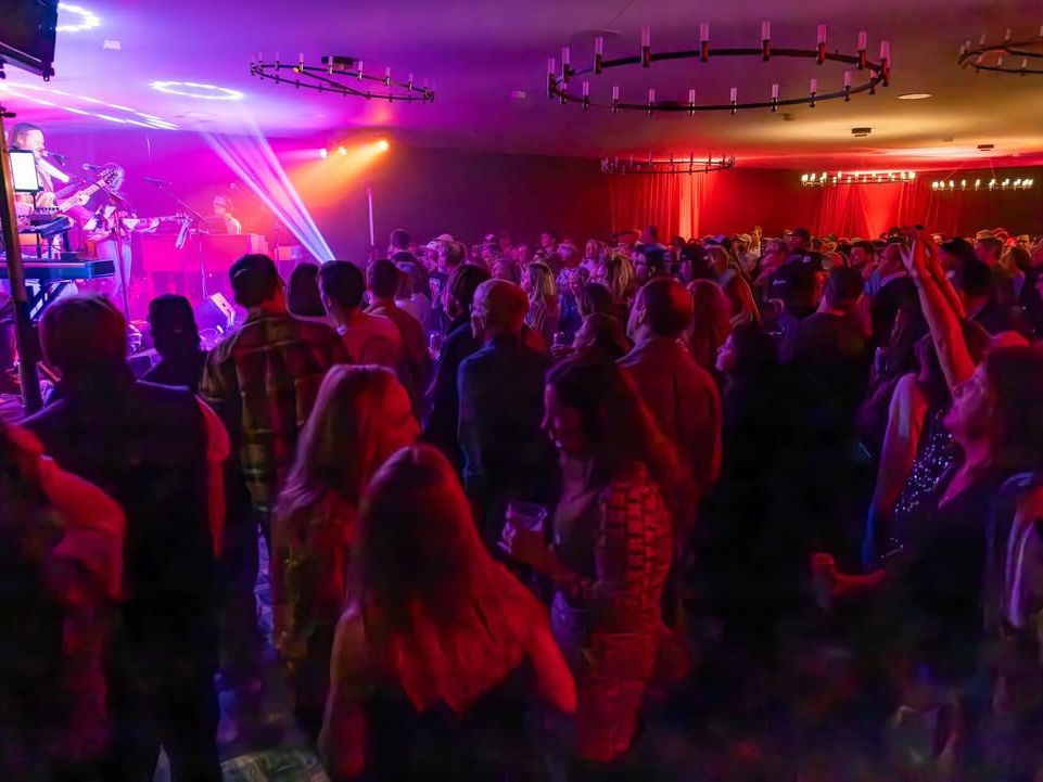 A packed crowd enjoys a live band performance at The Virginian Saloon, with colorful stage lights filling the room. This iconic Jackson Hole bar is known for its high-energy concerts, local music scene, and lively nightlife atmosphere.