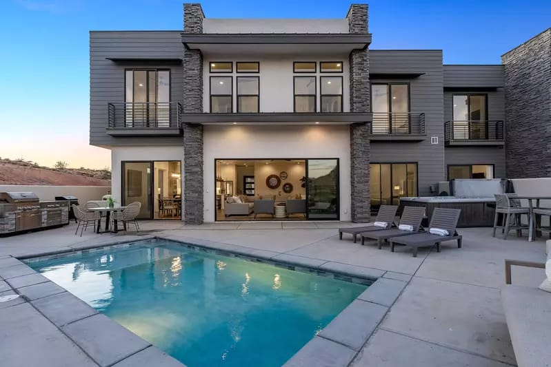Modern two-story home with large windows, a private pool, lounge chairs, and outdoor dining space.