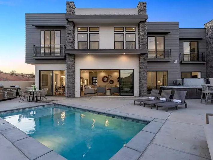 Modern two-story home with large windows, a private pool, lounge chairs, and outdoor dining space.