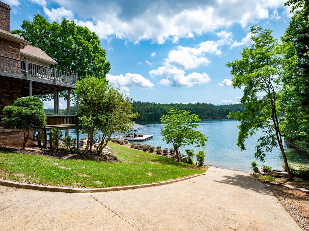 Aerial view of a wooded shoreline with private docks and boats resting on calm green water. The scene captures the charm of lakefront living in the Blue Ridge area, where adventure meets quiet relaxation