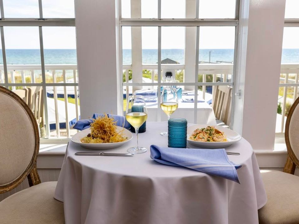 Romantic seaside dining at Beach Walk Café with white wine and plated seafood pastas by the window. Ocean views make this the perfect date night in Destin.