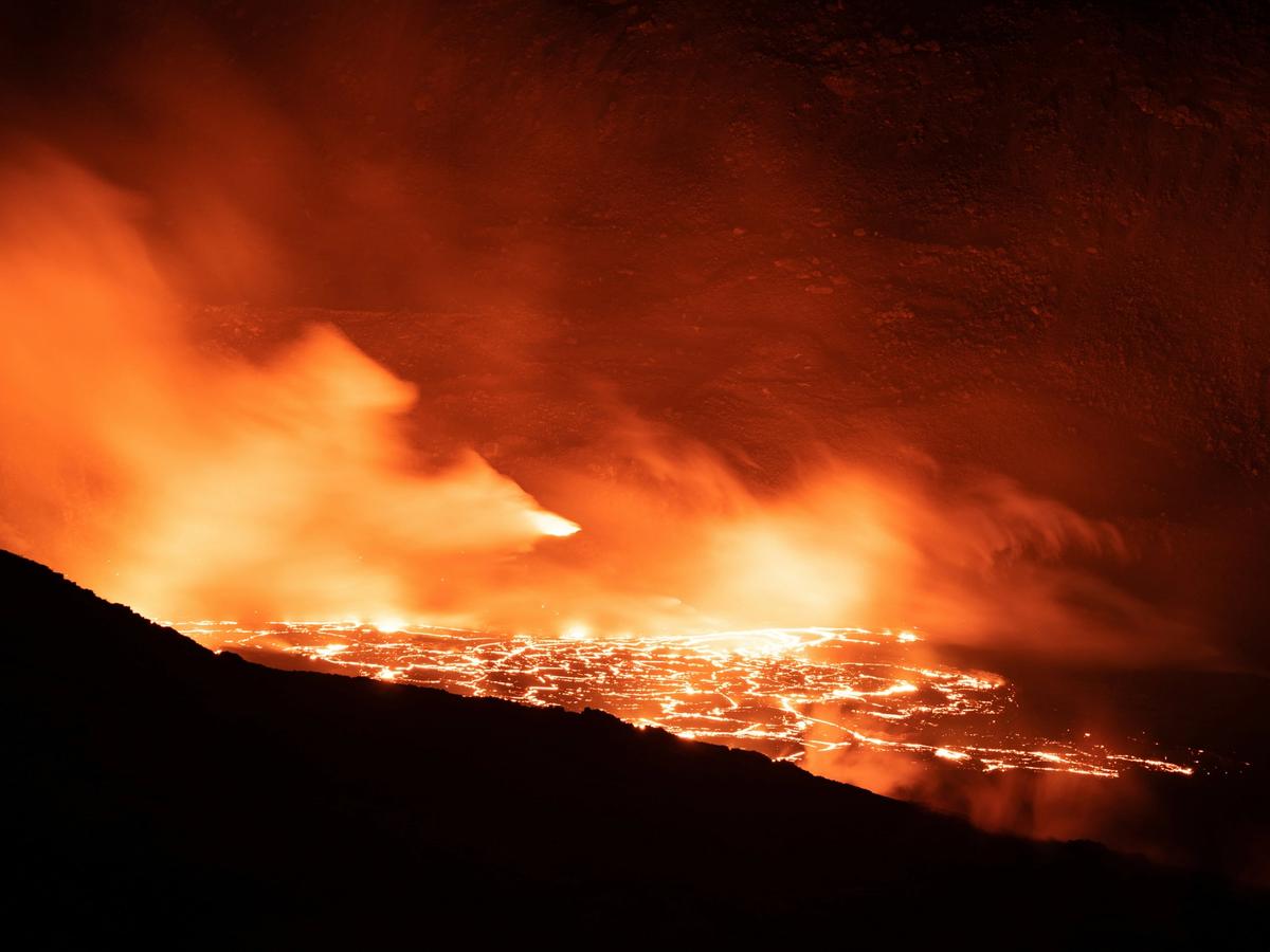 Bright molten lava glows and steams as it flows across the dark volcanic landscape, lighting up the night with fiery orange and red tones.