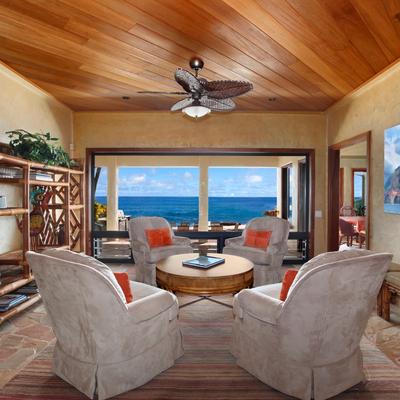 Cozy indoor seating area with plush chairs and a wooden ceiling fan, facing an open patio.