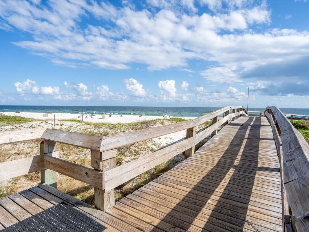 A quiet wooden boardwalk leads to the white sandy shores of Gulf Shores, Alabama, under a bright blue sky. Perfect for a peaceful last-minute beach escape without breaking the bank.