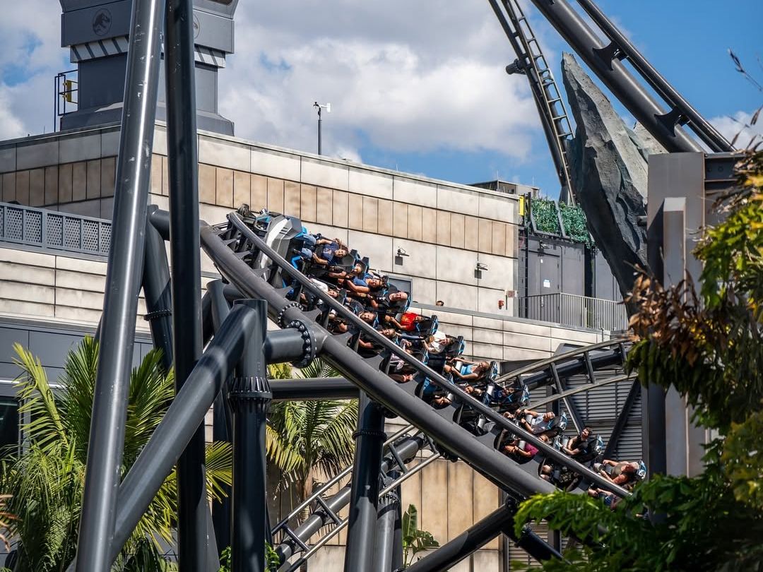 A packed roller coaster zooms through steep loops and sharp turns at Universal Orlando’s VelociCoaster ride. With palm trees and Jurassic World theming all around, this ride promises fast-paced fun for thrill seekers.