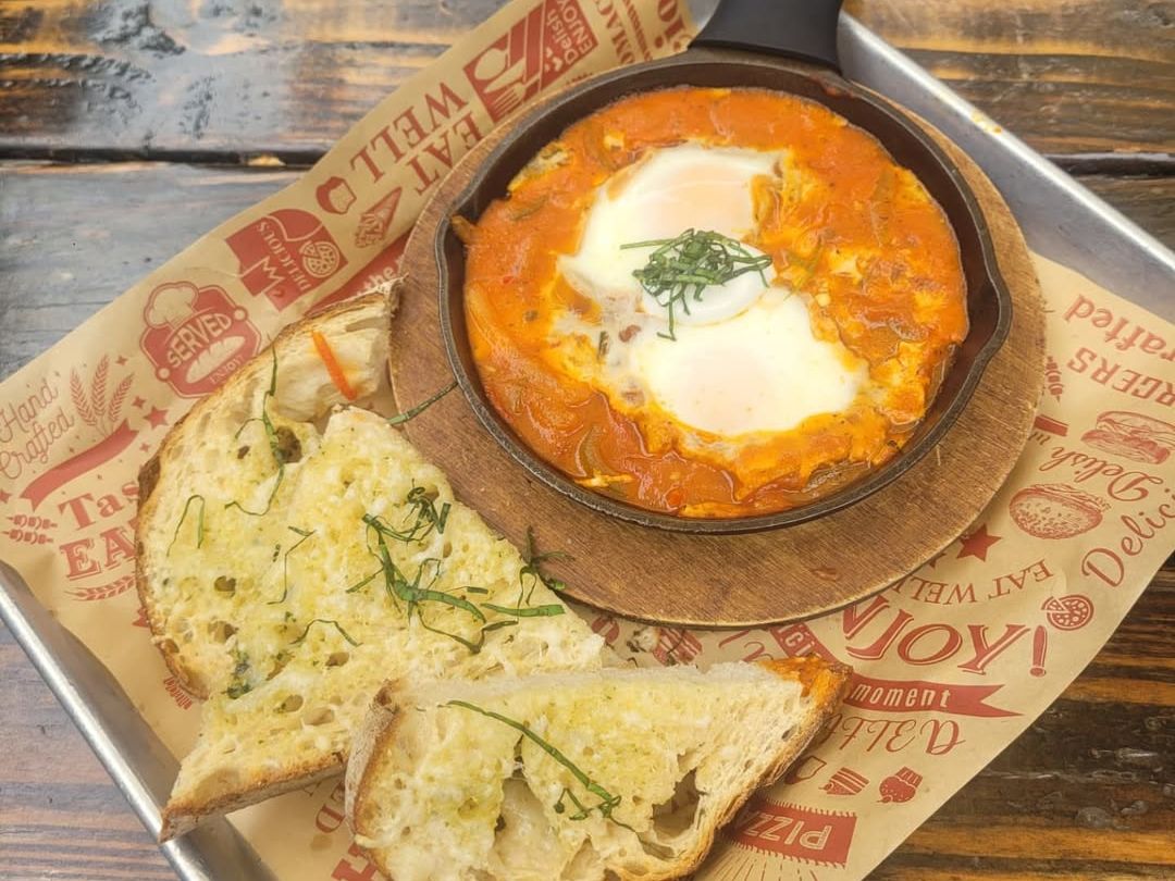 A skillet of baked eggs in rich tomato sauce is served with slices of toasted bread at Bayside Landing. This cozy comfort dish highlights the café’s rustic charm and casual dining vibe