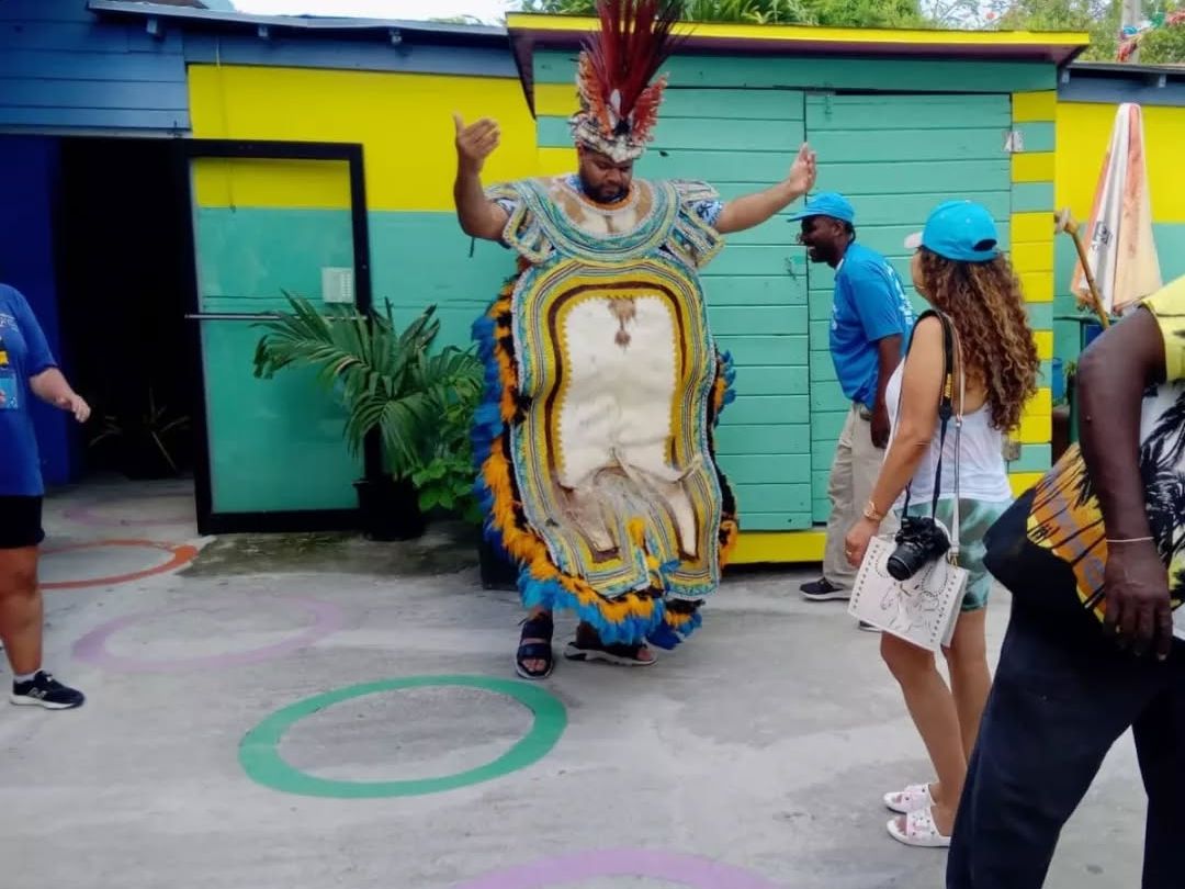 A Bahamian Junkanoo dancer in a colorful feathered costume performs in front of visitors. This vibrant street celebration is full of music, culture, and community spirit.