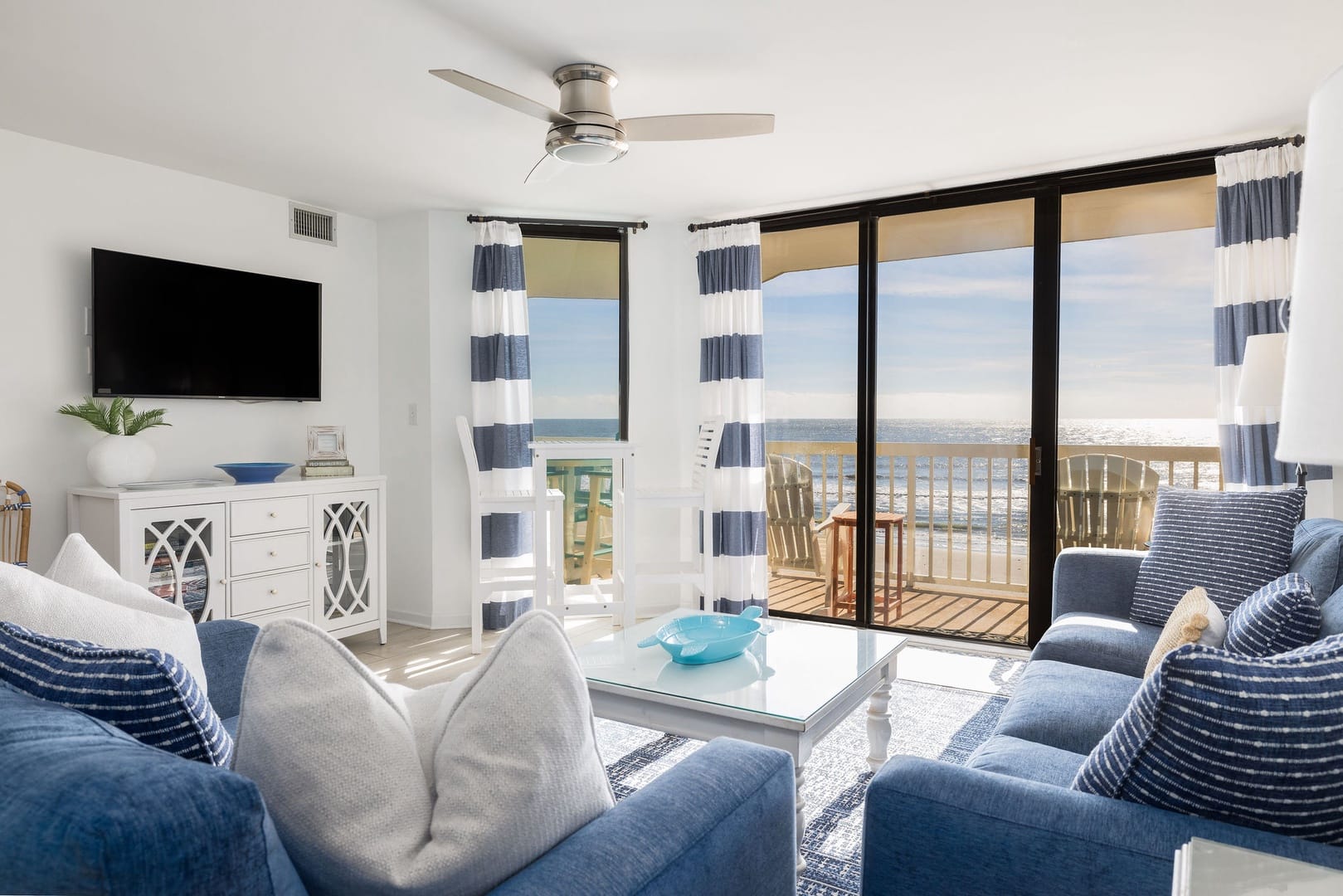 Interior living room with blue and white striped curtains and blue couches with ocean views