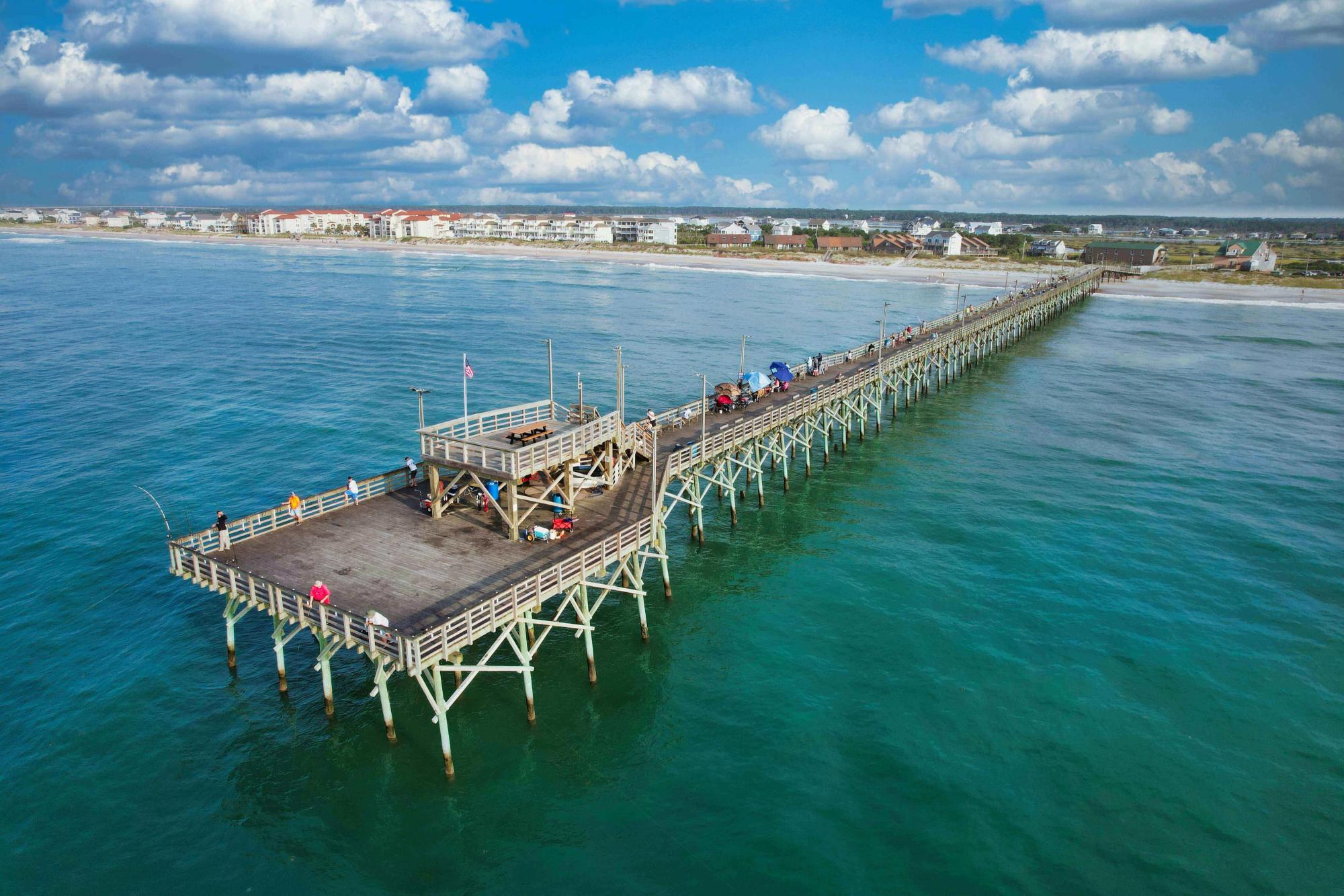 A long wooden fishing pier stretches over crystal-clear blue waters in Surf City, NC. Locals and visitors love this peaceful spot for casting a line, ocean views, and a breath of salty air.