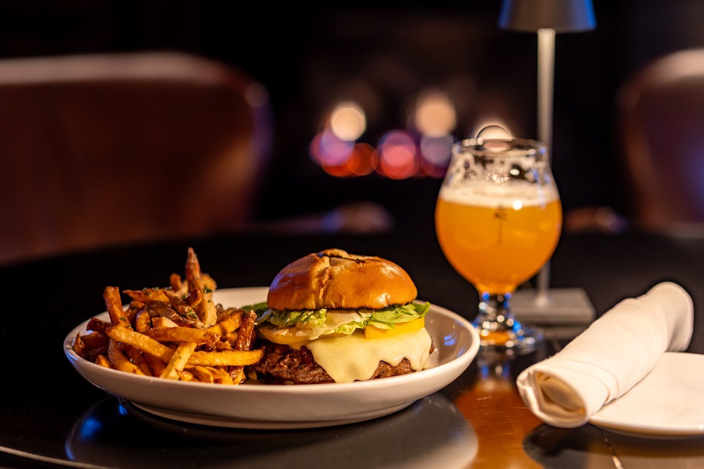 A classic burger with melted cheese and crispy fries served alongside a craft beer at Edson Hill in Stowe, Vermont. This cozy dining spot is known for elevated comfort food, a warm atmosphere, and a relaxed evening dining experience.