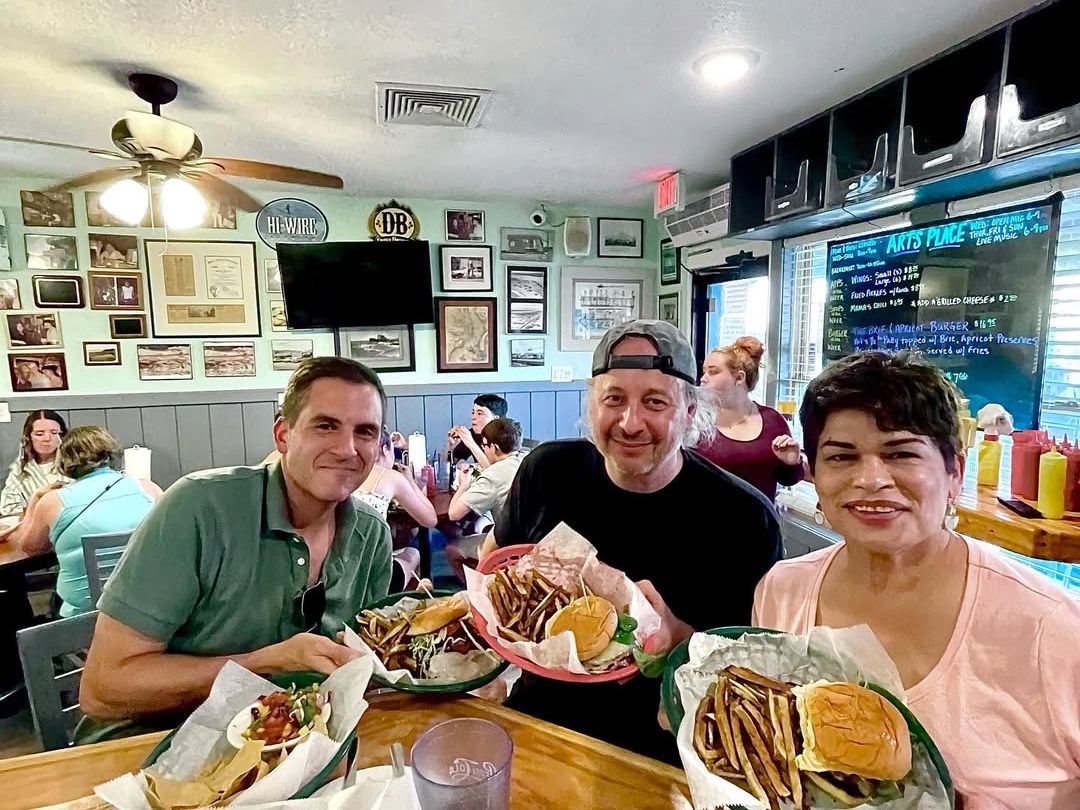 Three happy diners enjoy burgers, fries, and onion rings at Art’s Place, a casual local favorite filled with old-school charm. The cozy vibe, framed pictures, and handwritten chalkboard menu give it a true hometown feel.