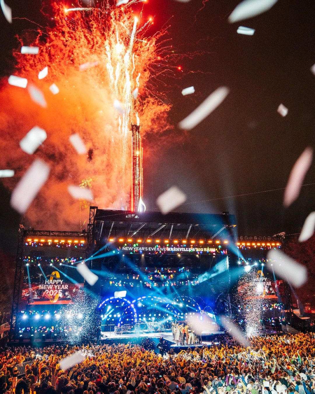 Fireworks explode above the Nashville Big Bash stage as confetti fills the air at midnight. The crowd celebrates the New Year with live performances and bright stage lights.